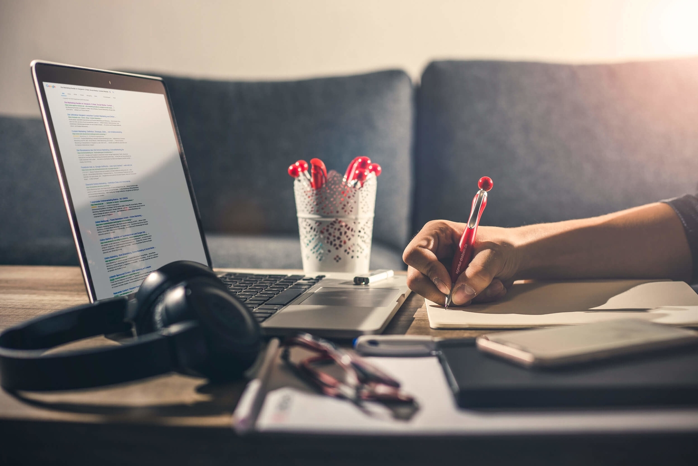 Laptop steht zusammen mit Blog, Kugelschreiber und Köpfhörer am Tisch.