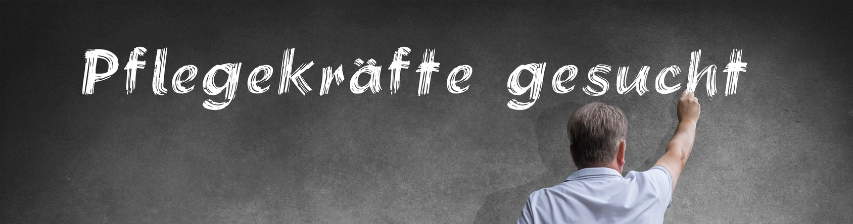 Mann schreibt mit Kreide "Pflegekr&auml;fte gesucht an die Tafel"