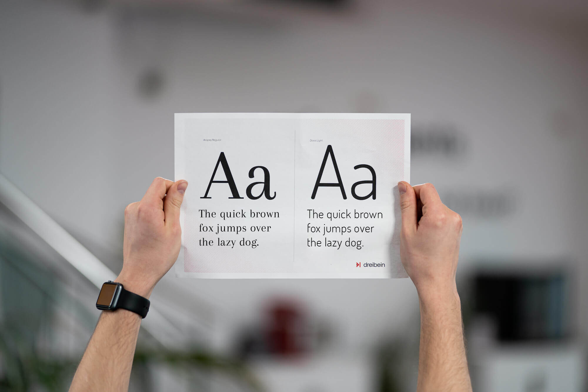 zwei Hände halten ein Blatt mit Typografie nach oben.